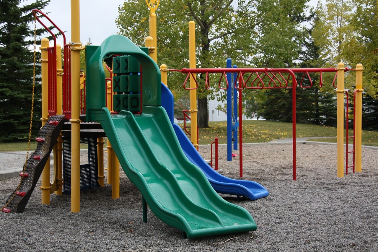Custom-designed playground structure featuring green and blue slides, climbing features, and safety surfacing, emphasizing inclusive outdoor play and recreation.
